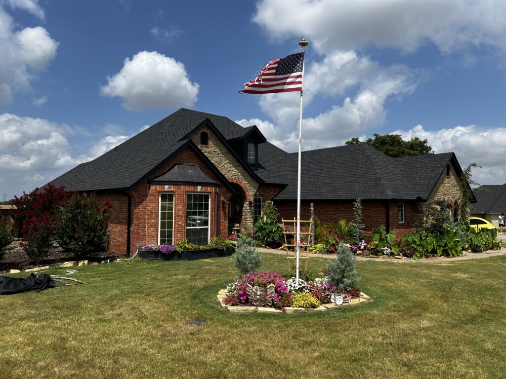 A brick home featuring a well-manicured garden and an American flag flying
