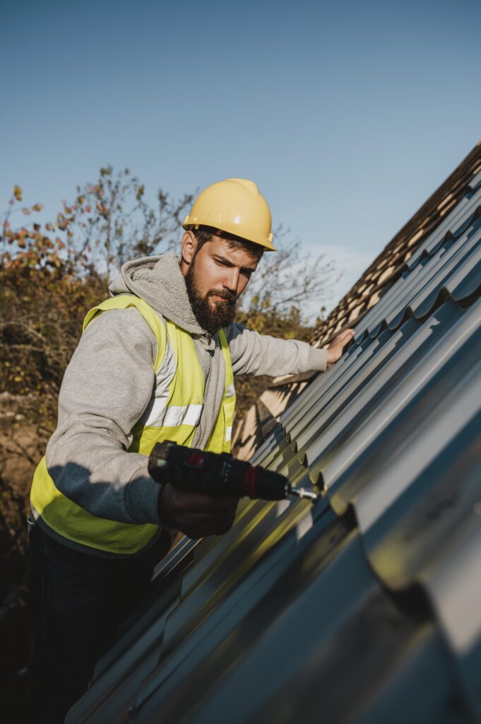 A man wearing a hard hat and safety vest is working on a roof, focused on his task in a construction environment.